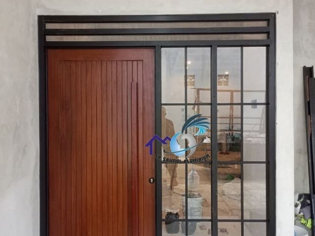 Pemasangan pintu utama kayu dengan kusen dan jendela ornamen aluminium hitam oleh CV. Sahrul Aluminium